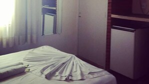 Una habitación de hotel con una cama, televisión, refrigerador y ventana con cortinas.