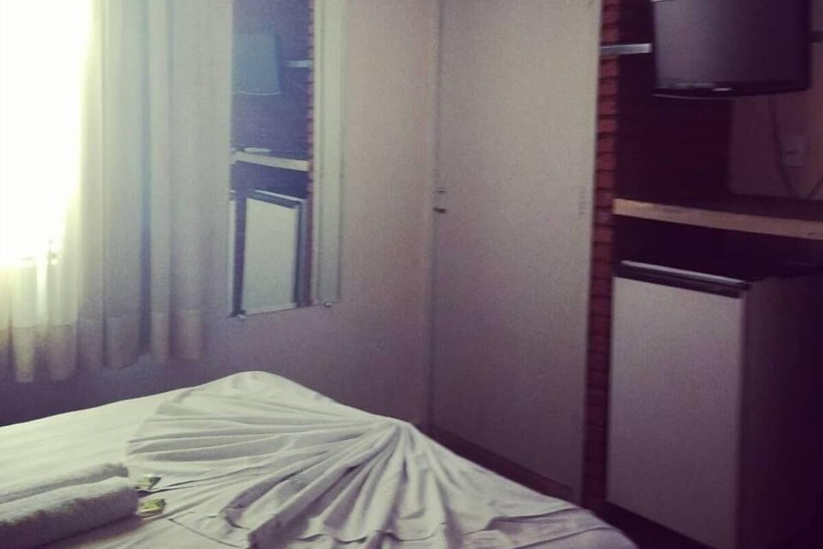 A hotel room with a bed, a television, a refrigerator, and a window with curtains.