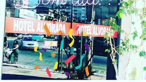 Entrada de un hotel con el letrero "HOTEL ALVORADA" y un mensaje festivo "Bom dia!" en la ventana.