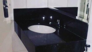 Un baño moderno con un mueble de tocador negro, un lavabo blanco y una cabina de ducha de vidrio.