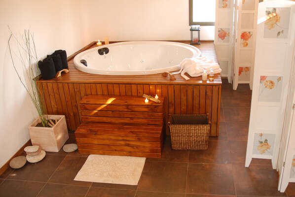 A wooden spa area with a hot tub, towels, a small plant, and a wicker basket.