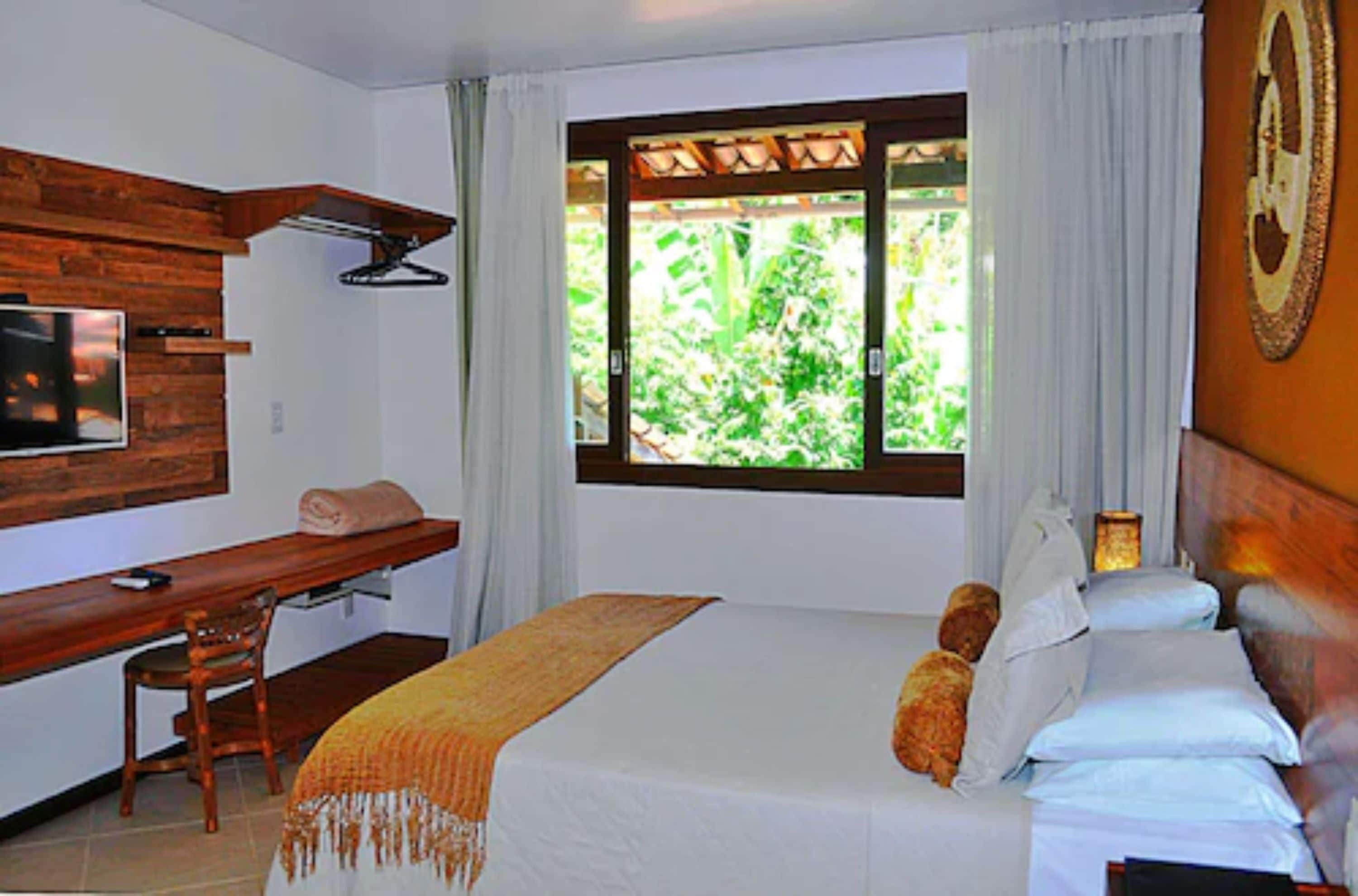 Un dormitorio con cama, escritorio, silla, televisor y ventana con cortinas.