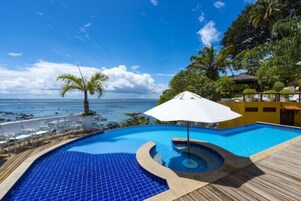 Piscina con vista al océano, rodeada de palmeras y una terraza de madera.