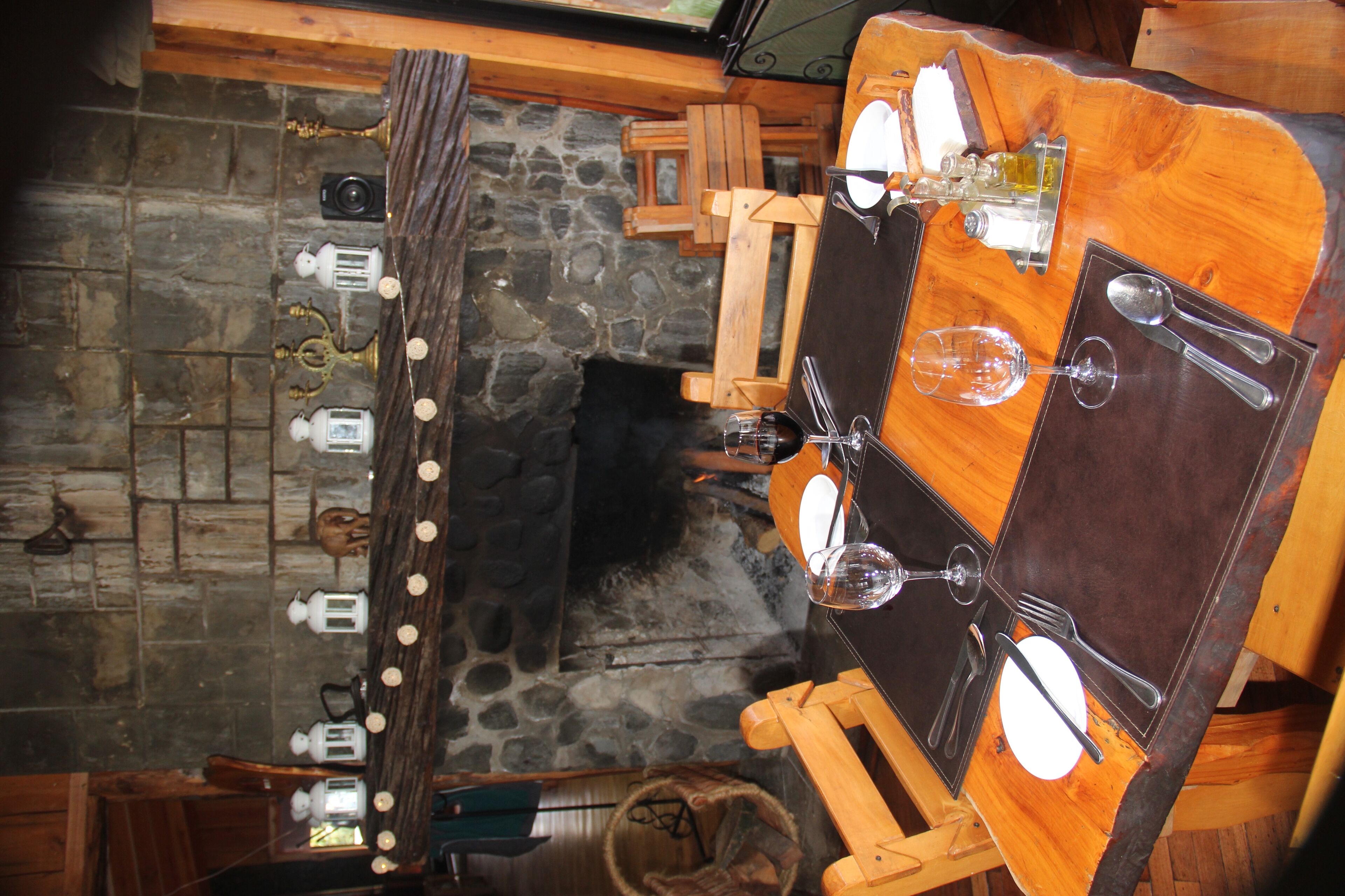 A rustic wooden table with a stone wall backdrop, equipped with a wine glass, a fork, a knife, and a spoon.