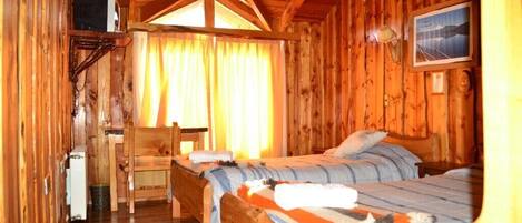 Una cabaña de madera con dos camas, un escritorio pequeño y una ventana con cortinas.