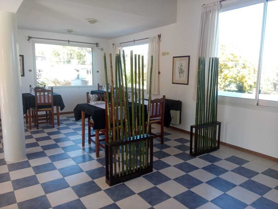 A room with a checkered floor, a dining table with chairs, and a window with curtains.