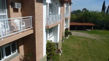Un edificio de varios pisos con fachada de ladrillo, balcones blancos y un pequeño jardín con césped y arbustos.