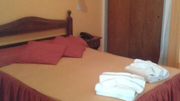 A neatly made bed with a wooden headboard, a bedside table with a lamp, and a door in the background.