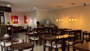 A restaurant with multiple tables and chairs, a bar area, and hanging pendant lights.