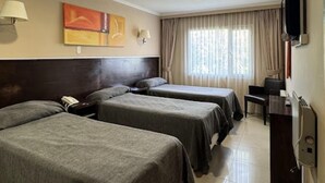 A hotel room with two single beds, a desk, a chair, a telephone, and a TV.