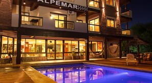 A two-story hotel with a pool area, outdoor seating, and a well-lit entrance. - Alpemar Apart Hotel & Spa Villa Gesell (Villa Gesell)
