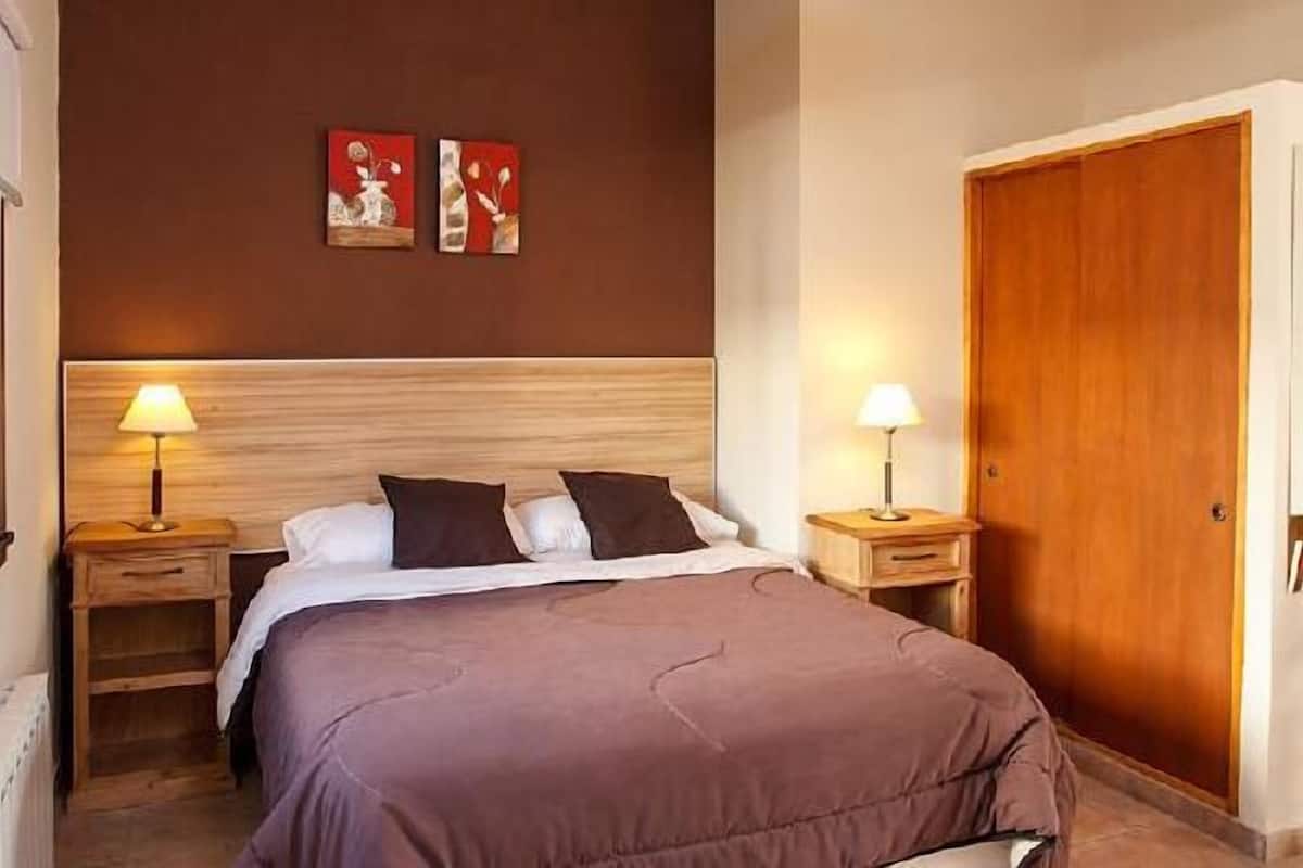 Ein Schlafzimmer mit hölzernem Kopfteil, zwei Nachttischlampen, einem Bett mit brauner Bettdecke und zwei an der Wand befestigten Bildern.