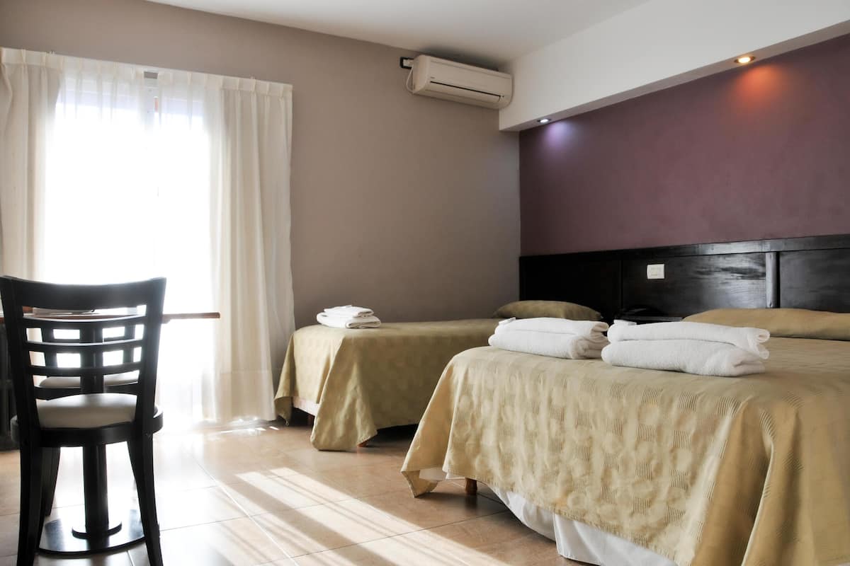 A hotel room with two beds, a desk, and an air conditioning unit.