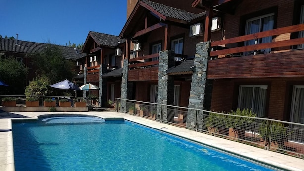 A swimming pool with a wooden deck, stone pillars, and a fenced area.