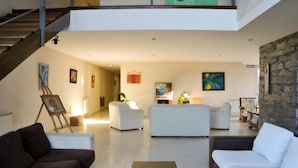 A spacious living area with a staircase, white sofas, a coffee table, and artwork on the walls.