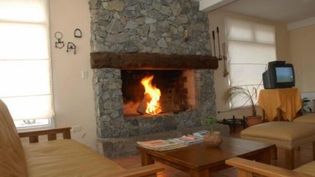 A living room with a stone fireplace, wooden furniture, and a television on a table. - Piedras del Lago (Tandil)
