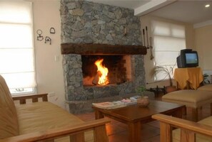 A living room with a stone fireplace, wooden furniture, and a television on a table. - Piedras del Lago (Tandil)
