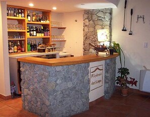 A bar area with a stone counter, shelves with bottles, glasses, and a sign reading "Picadores del Lago". - Piedras del Lago (Tandil)
