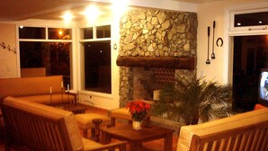 A cozy living room with a stone fireplace, wooden furniture, and a large window. - Piedras del Lago (Tandil)