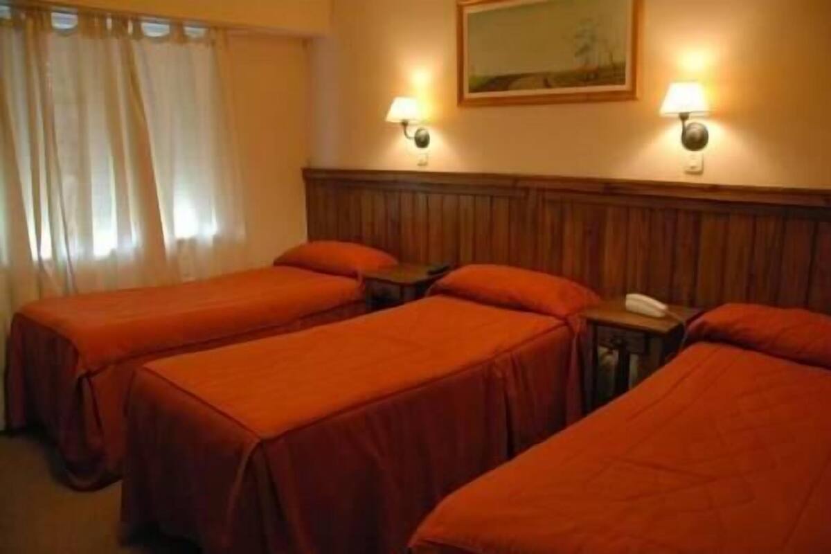 A hotel room with two single beds, a wooden headboard, two bedside lamps, a telephone, and a painting on the wall.