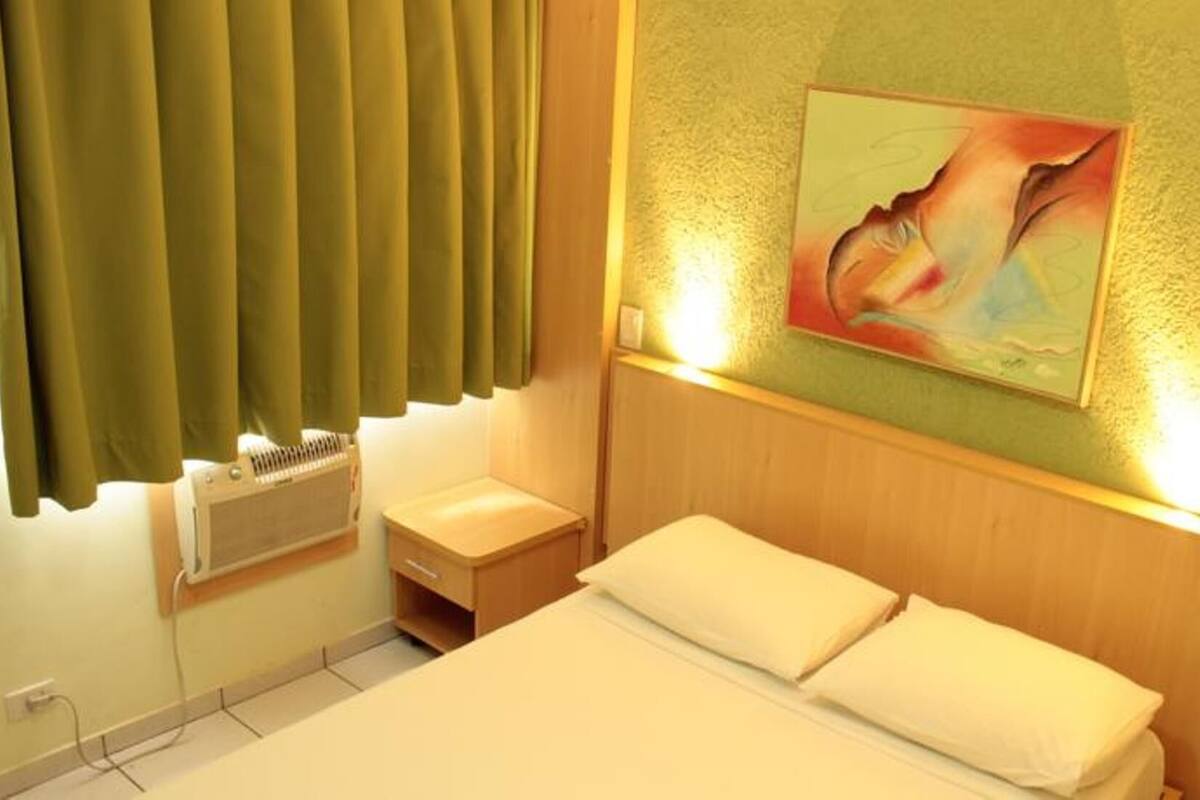 Quarto de hotel com cama, mesa de cabeceira, aquecedor na parede e um quadro.