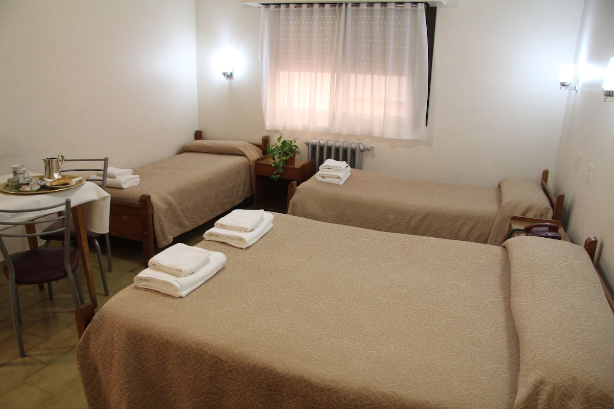 Une chambre d'hôtel avec deux lits simples, une petite table sur laquelle se trouve un plateau avec des articles pour le petit-déjeuner, une chaise et un bureau.
