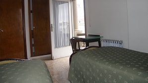 Een kamer met twee bedden, een houten deur, een raam met gordijnen, een tafel en een radiator.