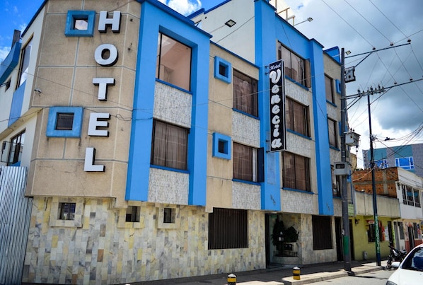 Un edificio de hotel con fachada azul y beige, múltiples ventanas y un letrero que indica que es un hotel.