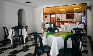 Un comedor con mesas y sillas, una cocina al fondo y un suelo a cuadros.