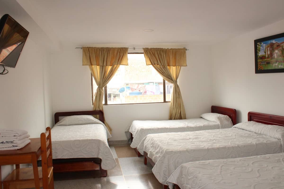 A hotel room with three single beds, a wooden desk, and a window with curtains.