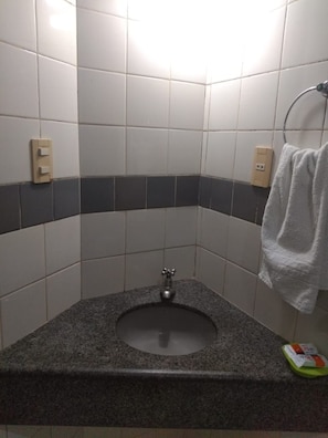 Une salle de bain avec un lavabo en granit, des carreaux blancs et gris, un porte-serviettes et un distributeur de savon.