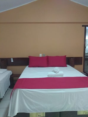 Un lit simple avec une couvre-lit blanche et rouge, deux oreillers rouges et une serviette blanche roulée posée sur le lit.