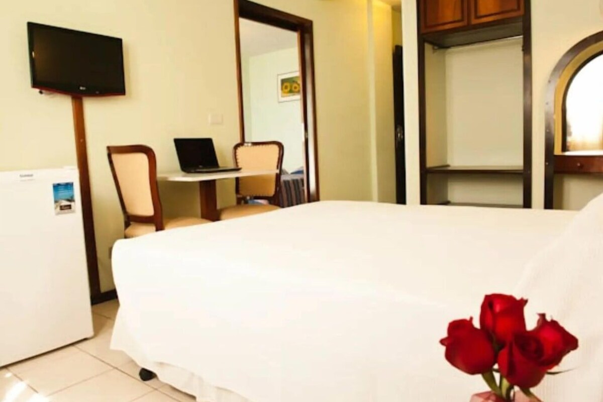 A hotel room with a bed, a desk with a laptop, a television on the wall, and a mirror.