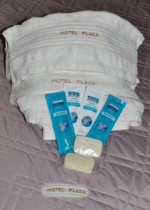 Una cama de hotel con toallas blancas y artículos de aseo, incluyendo champú y acondicionador.