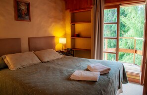 A bed with pillows, a bedside lamp, and a view of greenery through a window. - Hostería La Raclette (San Martin de los Andes)