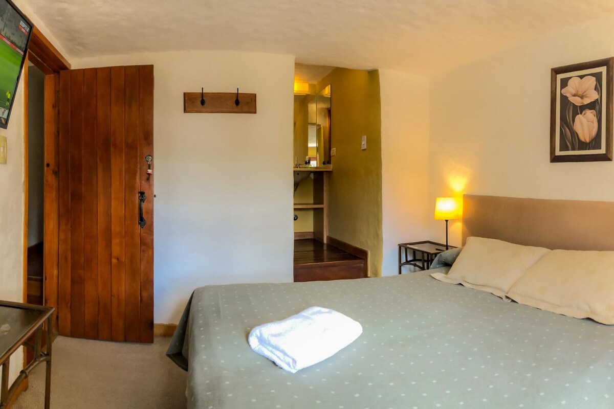 A hotel room with a bed, bedside lamps, a wooden door, and a small table.