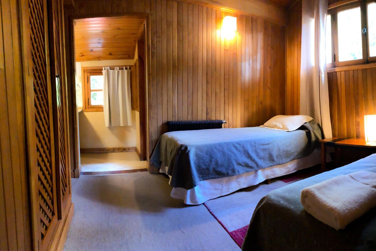 A wooden cabin room with a bed, a nightstand, and a window.