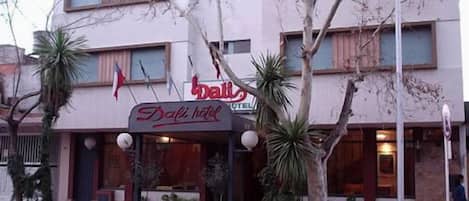 A hotel with a sign reading "Bali Hotel" and a palm tree in front.