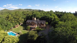 Una casa grande rodeada de bosque denso, con piscina y zona de patio.