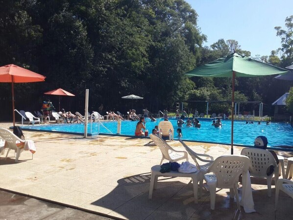 A swimming pool with lounge chairs and umbrellas, surrounded by trees.