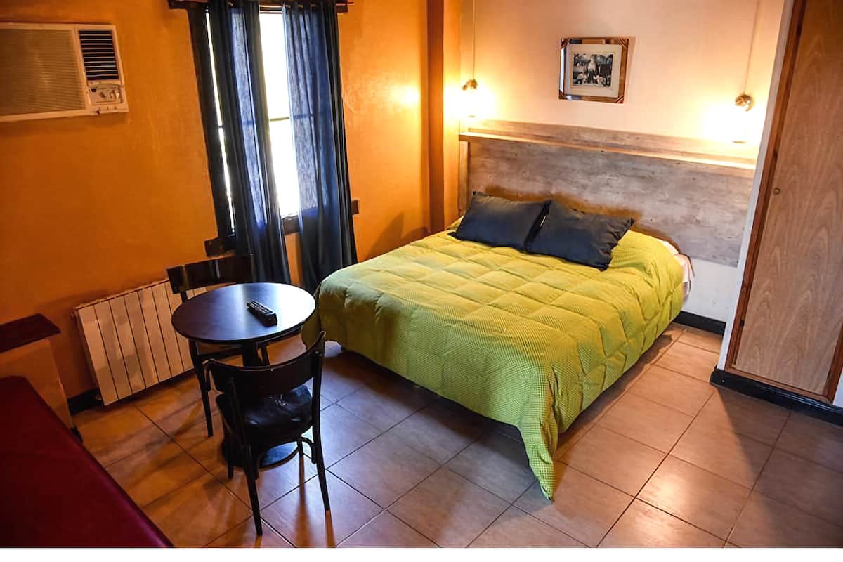 A room with a bed, a table, a chair, and a radiator.
