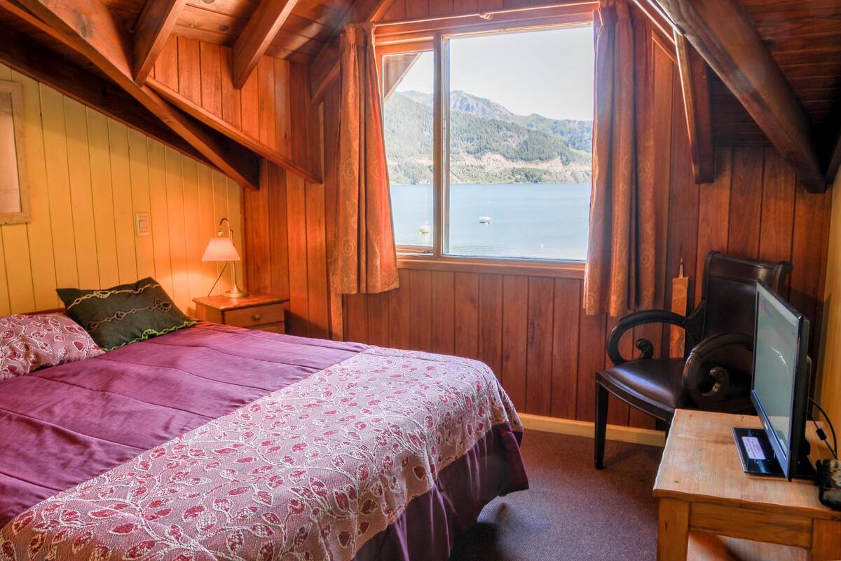 Ein Holzhütten-Zimmer mit einem Bett, einem Schreibtisch mit Computer und einem Fenster mit Blick auf einen See.