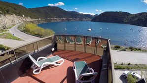A balcony with two lounge chairs and a table, overlooking a lake with boats and a mountainous landscape. - Valldemossa Apart Hotel (San Martín de los Andes)
