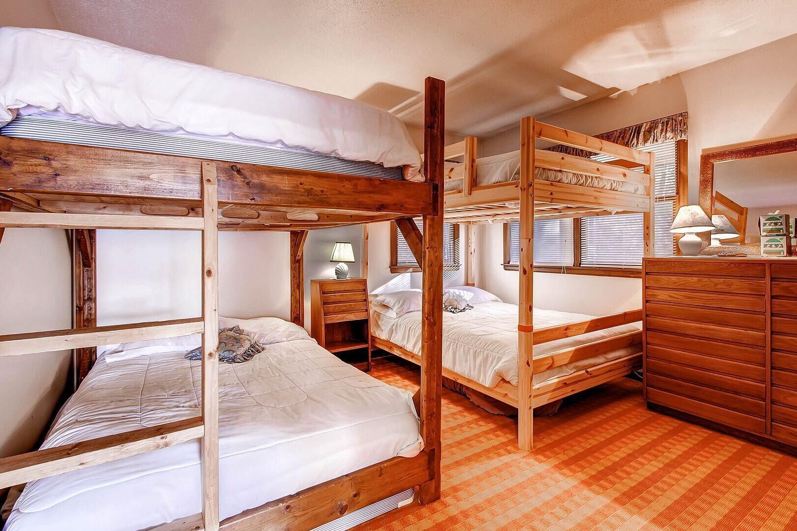 A bunk bed room with wooden frames, a dresser, and a lamp.