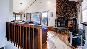 Una sala de estar acogedora con chimenea de piedra, suelo de madera y techo alto con vigas a la vista.