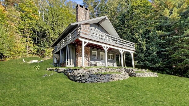 Una casa de dos pisos con base de piedra, un balcón y una chimenea.