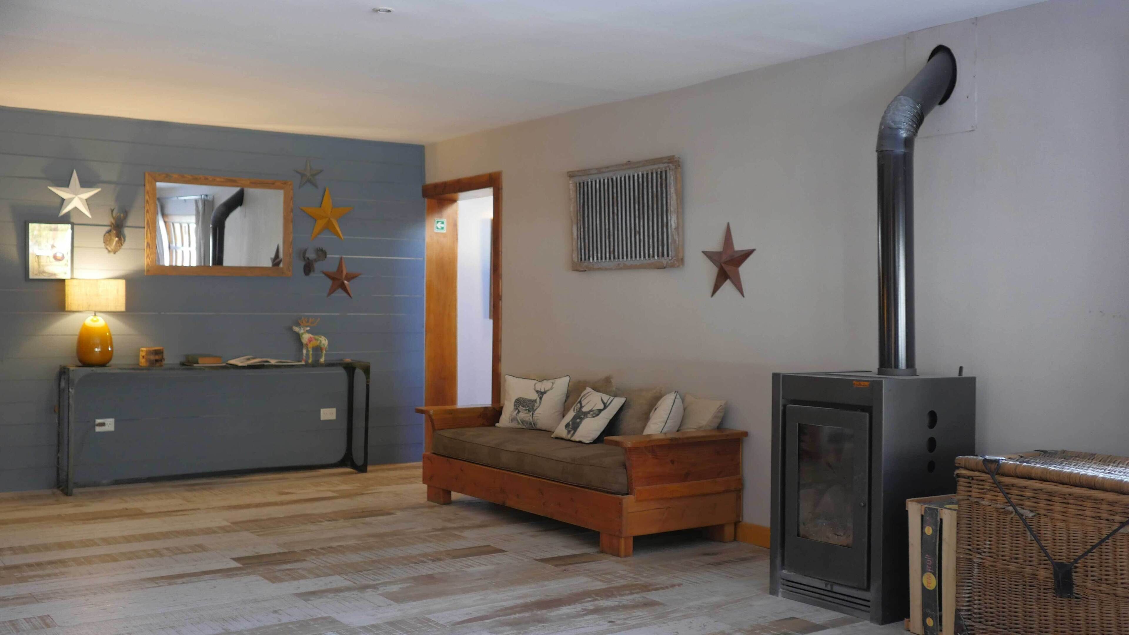 Ein gemütliches Wohnzimmer mit Sofa, einem kleinen Tisch mit Lampe, dekorativen Sternen, einem Kamin und einem Fenster mit Jalousien.