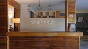 A reception desk with a wooden finish and a sign that reads "Soulmax". There are three pendant lights above the desk, and a bulletin board to the left. - Complejo Base 41 (San Carlos de Bariloche)