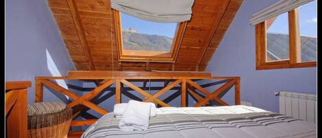 Un dormitorio con techo de madera, un ventanal grande, una cama y una silla de mimbre.