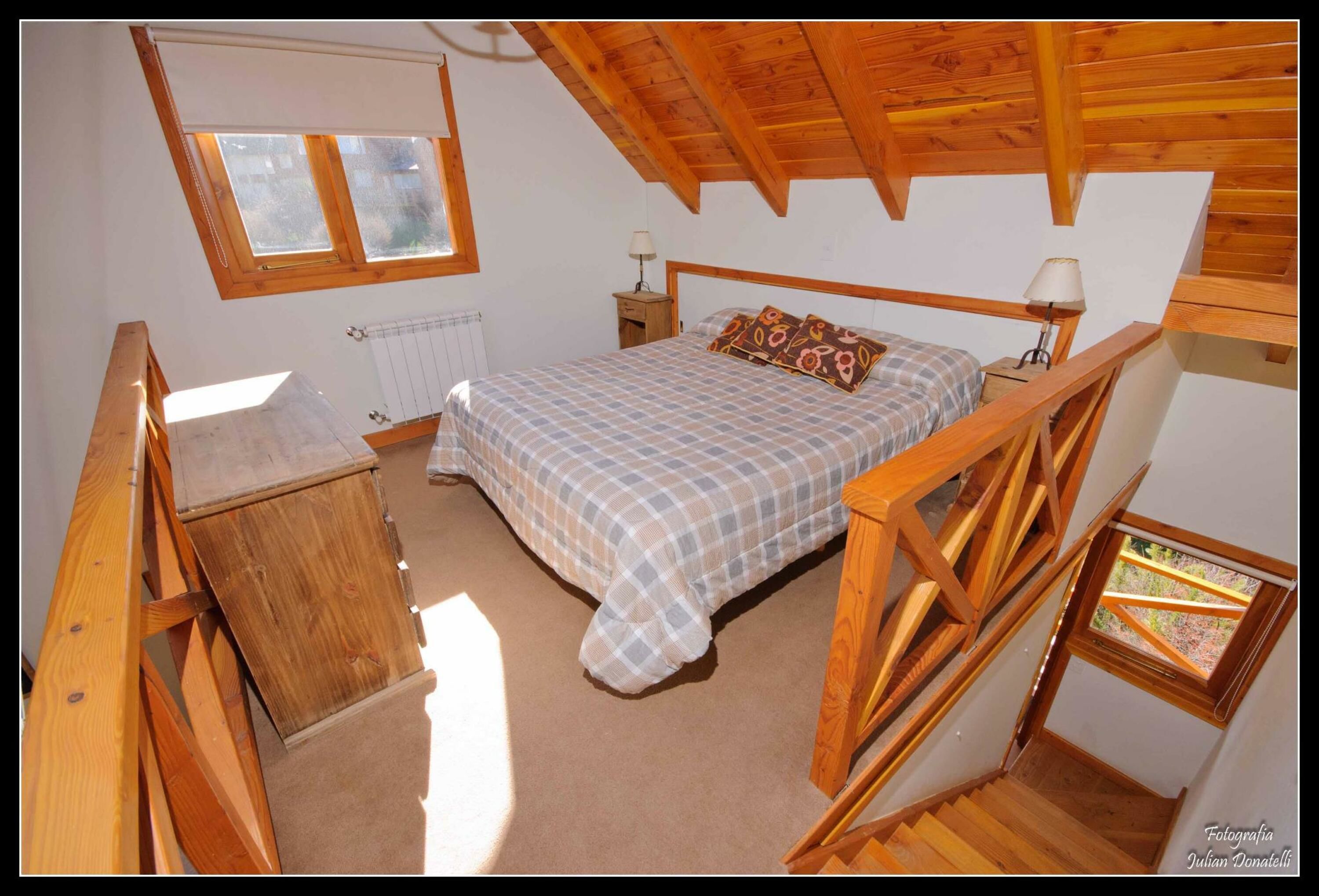 A bedroom with a bed, wooden headboard, two bedside tables with lamps, a window, and a radiator.